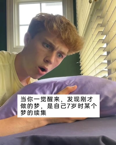 这是一张带有文字加注的真人情景图片，画面中一位穿着浅黄色上衣的金发男生，眼睛瞪大、嘴巴张开，满脸震惊，手放在紫色枕头上，姿态像是刚从睡梦中醒来。图片下方的白色框内配有文字：“当你一觉醒来，发现刚才做的梦，是自己7岁时某个梦的续集”，用夸张的表情演绎出人们在发现时隔多年的梦境被续上时的惊讶反应，这种奇特的梦境体验是很多人都有过的经历，容易引发大众的共鸣。