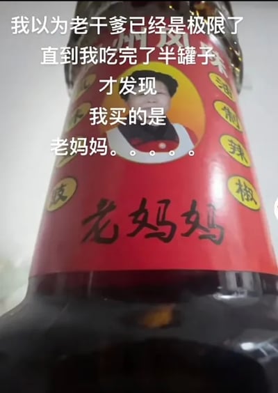 这是一张文字加注的静态实拍图，主体是一瓶名为“老妈妈”的油制辣椒酱，瓶身标签以红色为主，中部印有一位人物头像和醒目的“老妈妈”字样，瓶身右侧还有环形排列的“油制辣椒”文字。图上叠加了白色的吐槽文字：“我以为老干爹已经是极限了直到我吃完了半罐子才发现我买的是老妈妈。。。。。”，讲述了吐槽者原本觉得“老干爹”这类模仿“老干妈”的山寨辣椒酱已经很离谱，结果自己吃了半罐才发现买的是另一款山寨的“老妈妈”辣椒酱，充满了生活里买错商品的乌龙搞笑感，是对山寨食品的趣味调侃。