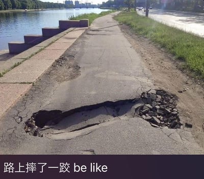 这张图展示了河边步道上一处严重破损凹陷的路面，路面的沥青层开裂塌陷，形成了一个类似被重物砸出的不规则大坑，旁边的步道和河景清晰可见。图片下方配有文字“路上摔了一跤 be like”，用真实的路面破损场景来夸张比喻人摔跤后的狼狈状态，仿佛摔跤的力道大到把路面都砸出了坑，通过这种视觉上的联想制造出搞笑的反差效果，生动地调侃了摔跤时的糗态。