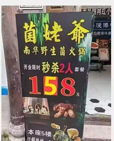 这是一张线下餐饮门店的开业宣传立牌，主体为黑色背景，搭配醒目的黄色、红色字体，顶部写有品牌名“菌姥爷”，下方标注品类“南华野生菌火锅”，核心宣传信息为“开业限时秒杀2人套餐158元”，价格数字用大字号红黄色突出显示，立牌下方配有野生菌的实物图片，底部标注店铺位置“本座5楼”及未显示完整的“订餐热线”。立牌背景中能看到其他店铺的部分招牌，显示出这是在商圈或美食街的线下场景，整体设计重点突出开业优惠，以低价套餐吸引路过的顾客，未使用双关、谐音梗等特殊内容。