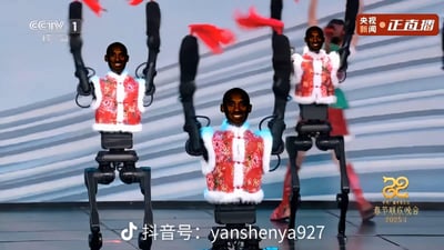 这是一张二次创作的合成图，创作者将已故篮球明星科比·布莱恩特的笑脸头像，替换到2025年央视春节联欢晚会舞台表演的机械机器人头部。机器人身着带有东北花棉袄风格的喜庆中式马甲，正挥舞着系有红绸的机械手臂，结合春晚的喜庆氛围与科比的头像，形成强烈的反差感，整体效果荒诞搞笑，充满玩梗趣味。