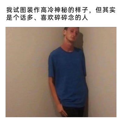 这是一张带有反差感的自嘲类静态梗图，图中上方配有文字“我试图装作高冷神秘的样子，但其实是个话多、喜欢碎碎念的人”，下方是一位穿着蓝色短袖的真人男子，他靠墙站立，身体姿态僵硬，头部歪斜，表情带着局促不自然的神态，外在故作疏离的高冷姿态，和配文里话多碎碎念的内在形成强烈反差，用幽默的方式自嘲自己在社交中的表里不一，很容易引发有类似社交伪装经历的人的共鸣。