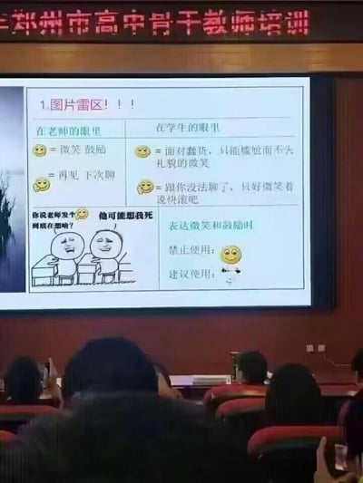 图片展示了郑州市高中骨干教师培训现场的投影屏幕内容。屏幕上是一张题为'图片雷区！！！'的幻灯片，通过对比表格呈现了老师与学生对同一emoji的不同解读。例如，老师眼中的😊是'微笑 鼓励'，而学生眼中则是'面对蠢货，只能尴尬而不失礼貌的微笑'；老师的'再见 下次聊'对应学生的'跟你没法聊了，只好微笑着说快滚吧'。幻灯片下方还有一幅卡通插画，描绘两人对话场景，并提示'表达微笑和鼓励时禁止使用：😊，建议使用另一emoji'。整个内容反映了师生间对网络表情符号的认知错位，具有幽默和警示意味，旨在提醒教师注意沟通中的表情符号使用规范。