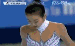 这是一段日本花样滑冰名将浅田真央在赛事中的动态图，她身着精致的亮片花滑比赛服，低头的姿态显示出她正处于比赛过程中，可能在完成动作间隙调整状态，画面带有赛事相关字幕，清晰展现了花滑赛场的专业瞬间。