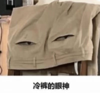 这张图展示了一条叠在椅子上的卡其色裤子，由于口袋的造型和阴影恰好形成了类似一双“冷漠的眼睛”的视觉错觉。画面下部配有文字“冷裤的眼神”，让裤子看起来像是有情绪的人脸，表达出一种“冷漠无语”的意味。属于典型的错位幽默网络表情包，画风幽默风趣，适合用来表达无语和吐槽心情。