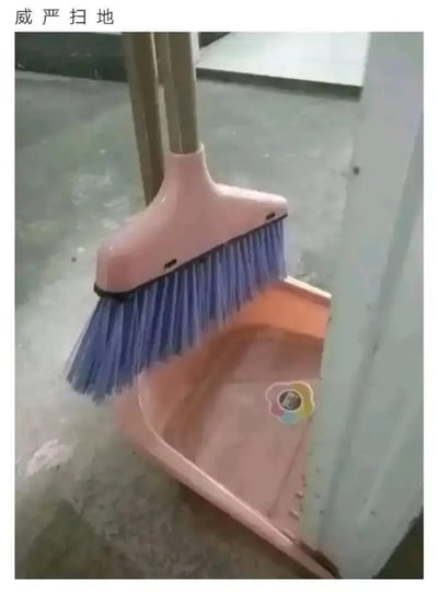 这张图片通过巧妙的拍摄角度制造了视觉错位效果，将靠在簸箕上的扫帚呈现出类似人叉腰站立的拟人化姿态。图片上方配有文字“威严扫地”，玩了谐音梗：一方面字面化地表现这个“拟人化”的扫帚仿佛带着威严的姿态在进行扫地动作；另一方面借用成语“威严扫地”的原意（形容威严完全丧失），形成反差感，让普通的清洁工具组合场景变得充满趣味，十分搞笑。