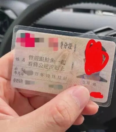这是一张经过人工修改的身份证照片，原本的证件信息被恶搞，姓名栏被改成了“曾經跟鮭魚一起看蔣公逆流而上”这样的超长且无厘头的内容，出生日期标注为1977年12月12日，性别为男，证件照片和部分信息被红色涂抹遮挡。该图片属于网络恶搞类创作，通过夸张、不符合现实的证件信息来制造荒诞搞笑的效果，在社交平台传播以博人一笑。