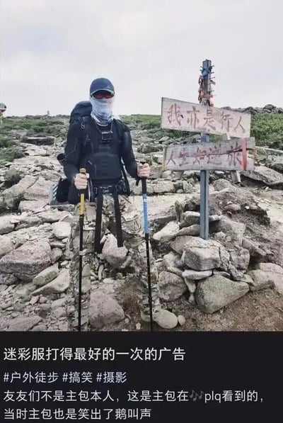 这张竖版搞笑实拍图呈现了户外山地徒步场景：一名身着全套户外徒步装备的男子站在布满石块的山地上，头戴帽子、佩戴墨镜和面罩遮挡面部，背着大容量登山包，双手各持一根登山杖，他穿着的迷彩裤的花纹和脚下的石滩外观高度相似，产生了男子下半身仿佛和地面融为一体、近乎“消失”的视觉错觉，男子身旁立有两块木牌，分别写有“我亦是行人”“人生如逆旅”的字样。图片底部黑色区域配有文字，调侃这是迷彩服效果最好的一次广告，附带#户外徒步 #搞笑 #摄影的话题标签，同时说明该图是发布者在评论区看到的内容，自己观看时笑得发出鹅叫。