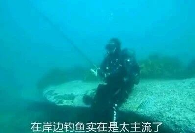 这是一张原始拍摄的横版真人图像，画面呈现了一位身着全套专业潜水装备的潜水员在水下环境中，手持钓鱼竿进行钓鱼的场景，画面底部配有字幕“在岸边钓鱼实在是太主流了”，通过将钓鱼场景从常规的岸边转移到水下，制造出强烈的反差感，以幽默搞笑的方式调侃传统钓鱼方式，展现出一种新奇另类的趣味钓鱼创意，整体构图清晰，水下的朦胧环境也让这个场景更具新奇感。