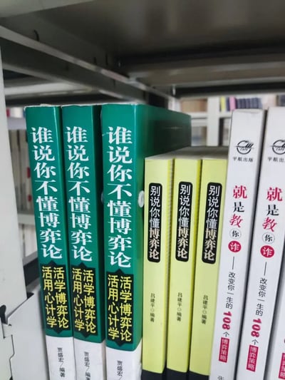 这是一张实拍书架的照片，书架上竖直排列着多本博弈论主题的书籍。从左至右依次为三本绿色书脊的《谁说你不懂博弈论》，副标题标注“活学博弈论 活用心计学”，编著者为贾盛宏；接下来是三本浅黄色书脊的《别说你懂博弈论》，编著者为吕建平；最右侧是两本白色书脊的《就是教你诈——改变你一生的108个博弈策略》，出版社标注为宇航出版。背景可以看到模糊的其他书架与书籍，整体构图清晰。