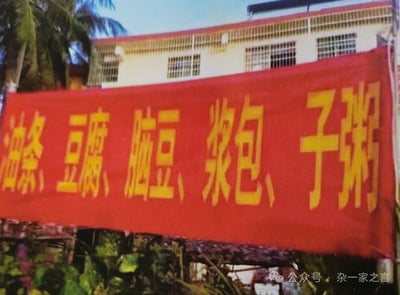 这是一张实拍的户外横幅照片，主体是一块红底黄字的横幅，横幅文字从左到右为「油条、豆腐、脑豆、浆包、子粥」，实际是商家制作横幅时错误拆分了早餐品类词汇，原本应该是「油条、豆腐脑、豆浆、包子、粥」，错版后形成了莫名其妙的内容，产生了搞笑效果。横幅背景可见一栋带多格窗户的浅色建筑、左上角的棕榈树以及下方的绿植，图片右下角带有「公众号：杂一家之言」的水印。