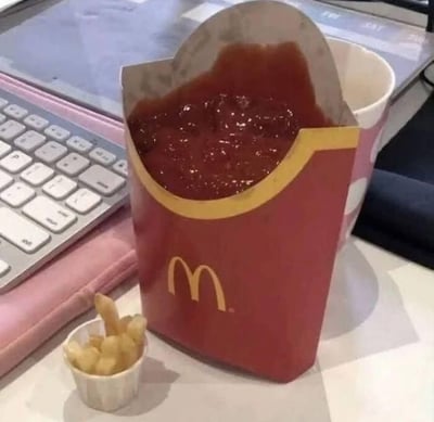 这是一张充满反差感的搞笑摆拍图：原本用来盛装薯条的麦当劳红色纸盒里被满满地装了番茄酱，而几根薯条却被放在旁边的迷你小纸筒中，完全颠倒了大众熟悉的薯条配酱的使用方式，通过反常规的搭配制造出荒诞搞笑的趣味效果。