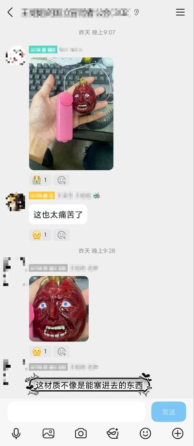 这是一张竖版的即时通讯软件聊天记录截图，聊天时间显示为前一日晚间：9点07分有匿名用户发出一张实拍图，图中手掌上托着两个物品，一个是粉色长条状电子物件，另一个是红色、表情扭曲狰狞、带有蓝色眼睛和眼泪、造型十分痛苦的人脸形状挂饰，背景可见键盘；随后有其他匿名用户回复文字“这也太痛苦了”；9点28分有匿名用户发出该红色痛苦脸挂饰的特写实拍图，紧接着有用户评论“这材质不像是能塞进去的东西”。界面还可见聊天的点赞表情按钮、底部的输入功能栏，所有发言用户的头像和昵称均做了打码处理。