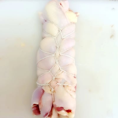 一张特写照片，展示了一块用白色棉线以交叉网格状捆绑的生鸡肉，放置在白色的砧板上。鸡肉呈现自然的淡粉色和白色脂肪纹理，肉质表面光滑，捆绑的棉线将肉块固定成规整的长条形状，可能用于烹饪前的定型处理。整个画面简洁，仅包含生鸡肉、棉线和砧板，无其他背景元素。