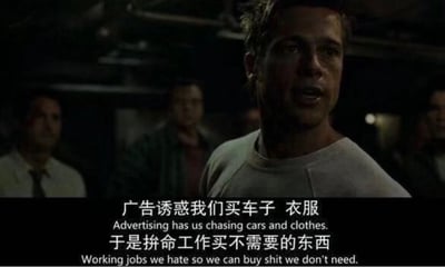 这是一张出自大卫·芬奇执导的电影《搏击俱乐部》的影视截图，画面场景为昏暗的室内空间，布拉德·皮特饰演的泰勒·德顿位于画面视觉中心，他穿着浅灰色上衣，神情激动，正面向身后的人群发表演说，身后的人物身影模糊，进一步突出了泰勒的主体地位。画面底部配有清晰的中英对照字幕，中文内容直指消费主义的陷阱：“广告诱惑我们买车子 衣服，于是拼命工作买不需要的东西”，英文则精准对应翻译，这段台词犀利地剖析了现代社会中人们被广告营销裹挟，为了购买非必需的商品而被迫从事自己厌恶的工作的荒诞处境，充满了对消费主义和异化职场的批判。