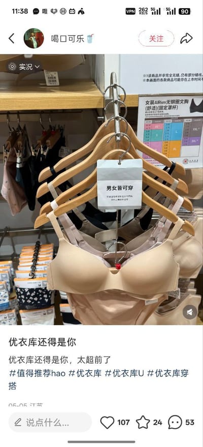 这是一张小红书平台的用户发布内容截图，发布者昵称为“喝口可乐”，内容拍摄自优衣库线下门店的内衣陈列区，陈列的女装AIRism无钢圈文胸上方悬挂着写有“男女皆可穿”的提示标牌，发布者配文调侃优衣库的产品设计理念过于超前，附带了多个优衣库相关的话题标签，该条内容获得了107赞、24收藏、53条评论的互动数据。