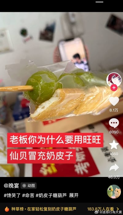 一张社交媒体截图，展示了一串用竹签串起来的绿色食物，看起来像是某种糖葫芦，下面垫着疑似旺旺仙贝的零食。图片上方有一部手机正在播放视频，下方有红色文字叠加：“老板你为什么要用旺旺仙贝冒充奶皮子”，表达了对食品用料的吐槽。截图显示该内容获得了8.1万点赞、8090条评论和46.0万次分享，带有#馋哭了 #命苦 #奶皮子糖葫芦 等话题标签。