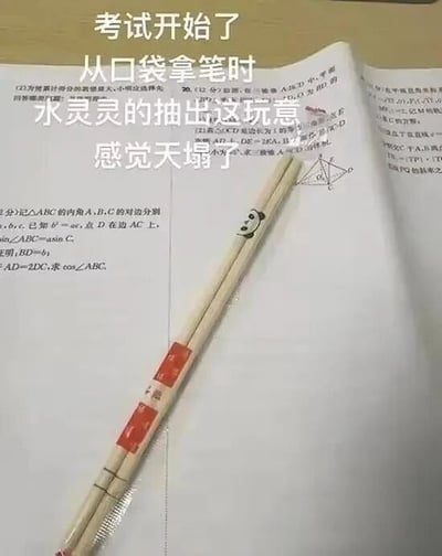 图片展示了一张摊开的数学考试卷，上面有几何题和三角函数题目（如涉及三角形边角关系的证明题）。试卷中央放置着一双带有红色包装纸的木质筷子，筷子顶端画着一个简笔画熊猫脸。图片上方叠加文字：'考试开始了 从口袋拿笔时 水灵灵的抽出这玩意 感觉天塌了'，通过错把筷子当笔掏出的意外场景，幽默表现考试时的慌张与尴尬，引发学生群体对考试突发状况的共鸣。