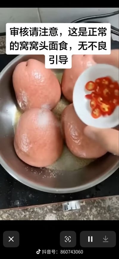 整张图是抖音短视频的截图，展示了烹饪窝窝头的场景，不锈钢锅中盛放着四个粉红色、外形酷似人体臀部的窝窝头，画面右侧有一只手正拿着盛有切好的红色小米辣的白色小碟子，准备往锅内添加配料。图片上方特意添加了白底黑字的提示文字，避免平台审核因食物外形产生误判，图片底部带有抖音的播放控制栏和对应发布者的抖音号标识。