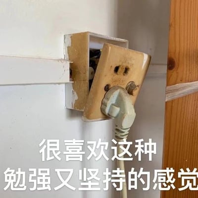 图片中展示了一个严重老化的插座：外壳泛黄破损，部分结构已从墙内脱出，露出内部线路，周围墙面有明显剥落痕迹。一个插头以倾斜角度勉强插入插座，呈现出“摇摇欲坠却仍在工作”的状态。图片底部配有白色文字“很喜欢这种勉强又坚持的感觉”，通过插座的物理状态隐喻生活中人们在困境中艰难维持的状态，形成强烈的情感共鸣。