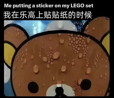 图片上方有中英双语文字“Me putting a sticker on my LEGO set / 我在乐高上贴贴纸的时候”，下方是卡通角色轻松熊（Rilakkuma）的特写画面。轻松熊的棕色脸部布满了水滴状的汗珠，双眼圆睁，表情看起来十分紧张，仿佛在进行一项需要极度小心、不容出错的任务，生动展现了人们在给乐高贴贴纸时生怕贴歪或损坏的焦虑心情。