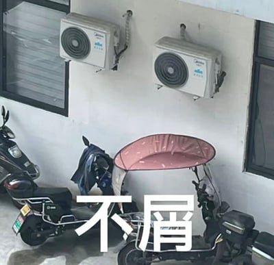 图片展示了一个室外角落场景，白色墙壁上安装着两台白色美的空调外机，下方停放着两辆电动 scooter。其中一辆 scooter 装有粉色带白色斑点的遮阳棚，整体环境像是居民楼或办公楼的走廊/停车区域。图片中央叠加了醒目的白色大字“不屑”，以幽默的方式赋予普通日常场景一种拟人化的轻蔑态度，营造出轻松搞笑的氛围。