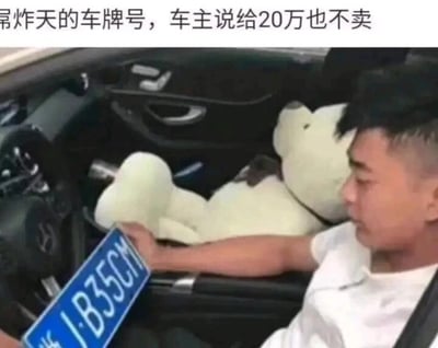 这是一张车内实拍的静态图片，画面中一名身着白色短袖的男子坐在奔驰汽车的驾驶座上，手中持有一块蓝色机动车车牌，车牌号码为“J·B35CM”。车内副驾驶位置放置着一个大型白色毛绒玩具。图片顶部配有文字“屌炸天的车牌号，车主说给20万也不卖”，该车牌号的谐音为“JB35厘米”，是带有低俗暗示的谐音梗，正是这个特殊的谐音让车主认为车牌很特别，即便有人出价20万也不愿意出售。