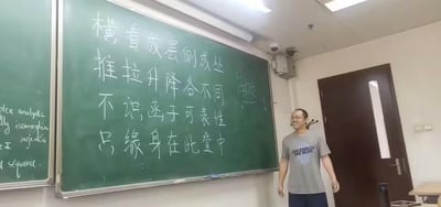 这是一张教室实拍图，画面里一位男老师站在黑板旁，脸上带着开心的笑容，看起来正和学生互动。黑板上写着改编自苏轼《题西林壁》的打油诗：“横看成层侧成丛，推拉升降各不同。不识函子可表性，只缘身在此叠中”，将原诗里描写庐山的内容替换成了数学范畴论中的专业概念，用大众熟悉的诗词形式调侃抽象的数学知识，降低理解门槛，充满趣味。旁边的小黑板上还写有“plex analytic”“isomorph”等英文数学相关词汇，进一步佐证这是数学课堂的场景。