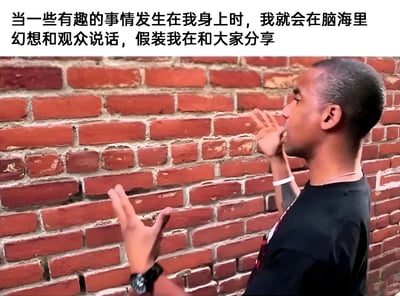 图片中一名黑人男性站在红砖墙前，侧身对着墙壁，右手抬起做出比划手势，左手也微微抬起，表情专注，似乎在对着墙壁说话。图片上方配有文字：'当一些有趣的事情发生在我身上时，我就会在脑海里幻想和观众说话，假装我在和大家分享'。这张图幽默地表现了人们内心丰富的戏精时刻，即使身边没有真正的听众，也会在脑海中构建分享场景。