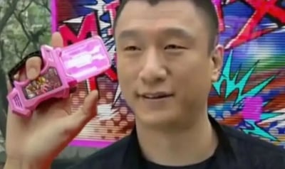 这是一张经过P图创作的趣味合成网络梗图，图中主体是中国内地演员孙红雷，他面带轻松的微笑，左手举着一个来自日本特摄剧《假面骑士Ex-Aid》的粉色骑士转玩卡带，该卡带是剧中角色变身的核心道具；背景是带有涂鸦风格的彩色图案，和卡带的特摄风格相呼应。这张图将现实知名演员的形象与热门特摄IP的关键道具结合，利用形象反差制造出无厘头的搞笑效果，属于网络二次创作的搞笑内容，在ACGN社群和网络社交平台中传播，用来制造趣味话题。