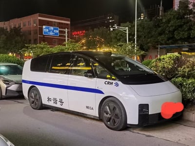 夜晚的河南长葛街头，一辆理想MEGA MPV完成了极具创意的个性化涂装改装：车身以和谐号高铁的白蓝黑配色为模板，白色车身搭配黑色车顶，一条蓝色腰线贯穿车身侧面，车身印有“和谐号”字样，车头侧方标注了高铁的“CRH”标识与和谐号专属标志，原本主打家用的MPV瞬间拥有了高铁的辨识度，反差感拉满，创意十足。背景能看到城市街道的路牌、绿植和其他车辆，呈现出日常的城市夜景。