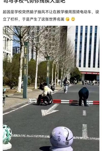 这是一张拍摄于校园的搞笑照片，学校为禁止电动车在教学楼周边通行，设置了低矮的红白栏杆。画面中一名学生坐在轮椅上，试图从栏杆下方钻过去，旁边还有一人弯腰摆弄栏杆，远处有不少学生围观。搭配上方的吐槽文字，用极具反差感的行为调侃学校突然出台的不合理规定，讽刺栏杆的设置仿佛只允许残疾人通行，引发共鸣。