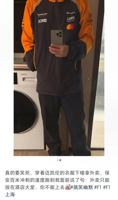 该内容为图文混排的社交媒体分享内容，上半部分是对镜自拍的静态照片，画面为镜像状态因此衣物上的标识均为反向，仅露出拍摄者颈部以下的身体，拍摄者穿着橙黑配色的迈凯伦F1车队外套与同色系长裤，手持苹果手机拍摄，身后可见一台滚筒洗衣机；下半部分是配文，讲述发布者穿这件外套下楼拿外卖时，被酒店保安误认成外卖骑手，保安上前告知外卖只能放在酒店大堂不能上楼的搞笑乌龙经历，还附带了相关话题标签。