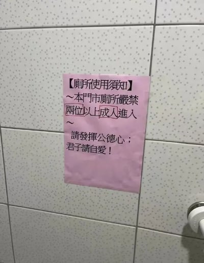 一张拍摄于门市厕所内的照片，白色带点瓷砖墙上贴着一张粉色告示，标题为【厕所使用须知】，内容规定"本门市厕所严禁两位以上成人进入"，并附有"请发挥公德心；君子请自愛！"的提示。这种特殊规定让人不禁猜测背后可能存在的奇葩使用场景，带有明显的幽默和讽刺意味。