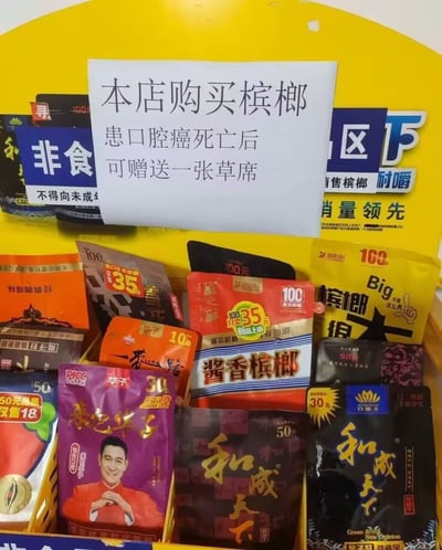 图片展示了一家商店槟榔展示柜，上方贴有一张引人注目的纸质告示，内容为："本店购买槟榔，患口腔癌死亡后可赠送一张草席"。这种极端直白、黑色幽默的标语用戏谑手法讽刺了嚼槟榔对口腔健康的严重危害，而且“草席”通常用作丧葬象征，进一步加深死亡双关梗，引发强烈反差和记忆点。

此图片明显有玩笑和警示的双重意味。

- 暗示/双关：告示用“死亡后赠草席”幽默批判槟榔危害，用极端后果来劝阻消费，引发网络讨论。
- 无明显谐音梗。