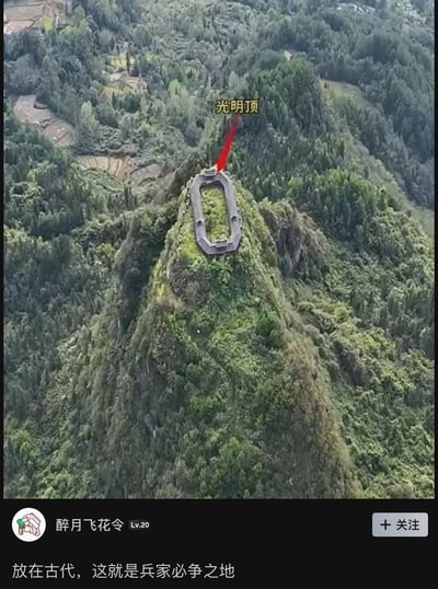 这是一张航拍视角的山地照片，画面中央是一座被茂密森林环绕的陡峭山峰，山顶上有一个规则的长方形堡垒式建筑。建筑上方有黄色文字标注"光明顶"，并有一条红色箭头从文字指向建筑。图片底部显示了社交媒体评论界面，用户"醉月飞花令(Lv.20)"评论道："放在古代，这就是兵家必争之地"。整个场景展现了一处地势险要的山顶建筑，通过文字标注和评论形成了历史与现实的趣味联系。