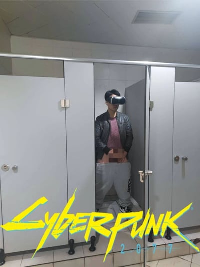 这是一张经过P图改编的静态实拍照片，场景设定在公共厕所的隔间内：一名男子佩戴着VR眼镜与耳机，站在隔间中，裤子下拉至大腿位置，隐私部位被打码处理。图片下方添加了知名科幻RPG游戏《赛博朋克2077》的黄蓝配色标志性logo，通过将日常私密场景与VR设备、游戏IP结合，营造出荒诞搞笑的反差感，以此恶搞“沉浸式体验赛博朋克世界”的概念，调侃玩家对游戏的沉迷或是游戏里的各类场景。