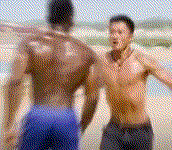 这是截取自动作电影《战狼2》的动态画面，画面中吴京饰演的冷锋赤裸上身，在沙滩上面对一位黑人男性，大张着嘴，情绪十分激动，呈现出愤怒对峙的状态。该画面常被用作梗图，用来表达激动、愤怒、与人争执时的情绪。