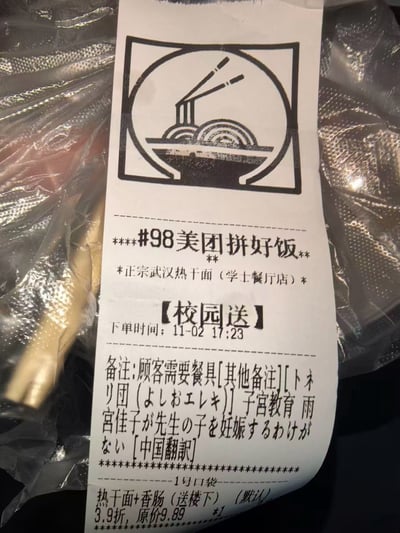 这是一张美团拼好饭的外卖订单收据，主要内容是一份正宗武汉热干面。收据上方有一个简单的面条和筷子图案，中间显示了订单信息，包括商家名称（学士餐厅店）、下单时间（11月2日17:23）和具体商品（热干面+香肠）。特别引人注意的是备注栏中除了正常的餐具需求外，还夹杂了一段日文文本和中文翻译，内容看起来有些奇怪和不相关。