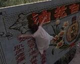 图片中展示一面户外墙壁，墙面上有红色的'油糕'文字及一些装饰图案，一名穿着浅色衣物的人正攀爬在墙壁上，身体前倾，似乎在靠近墙上的文字或图案。墙壁背景略显陈旧，整体场景给人一种生活化的户外即视感。