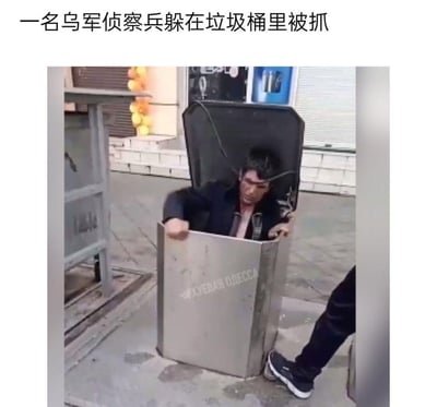这张图片是一段视频的截图，画面中一名神情狼狈的男子正从一个金属垃圾桶里探出身，双手扶着垃圾桶的边缘，旁边还有另一个人的部分身影。图片上方配有文字称该男子是“一名乌军侦察兵躲在垃圾桶里被抓”，垃圾桶正面印有俄文标识，场景发生在户外的街道区域，整体氛围显得窘迫。