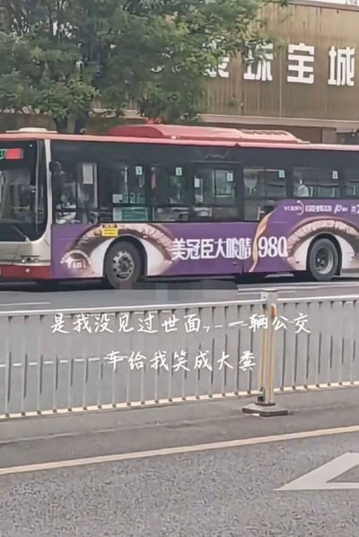 这是一张拍摄于城市街道的实拍照片，画面主体是一辆行驶中的公交车，车身印有美冠臣眼部项目的商业广告，广告设计的大眼睛图案恰好与公交车的车轮位置重合，车轮看起来像是眼睛的瞳孔，形成了极具趣味的视觉错位效果。图片下方配有白色文字“是我没见过世面，一辆公交车给我笑成大粪”，表达了拍摄者看到这个巧合画面后的调侃心情。背景中可以看到路边的树木，以及写有“珠宝城”字样的临街建筑，公交车内还能看到模糊的乘客身影。