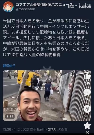 这是一张搬运自推特的社交媒体截图，推特用户@roaneatan用日文发帖爆料，称有中国博主在美国经济宽裕的情况下，冒充日本人领取给贫民的救济食物，还进行反日活动，仅一天就跑了10个点位获取大量饮食，指责其抢夺美国贫民的资源。帖子附带一段实拍视频的截图，视频里该博主在美国街头对着镜头大笑，背景可见黄色校车和街头行人，展现了当地的街景。