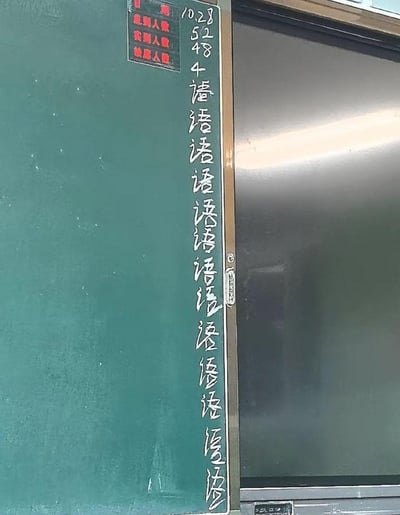 这是一张校园教室场景的实拍图，画面左侧是绿色黑板，黑板右侧边缘用白色粉笔写着日期“10.28”，以及数字“52 48 4”，对应黑板上方红色考勤牌的应到人数、实到人数、缺席人数。数字下方是重复书写的大量“语”字，推测是4名缺席的学生被老师惩罚抄写“语”字，以此作为缺席的处罚，画面传递出学生被罚抄的无奈感，图中没有双关、谐音梗或暗示内容。