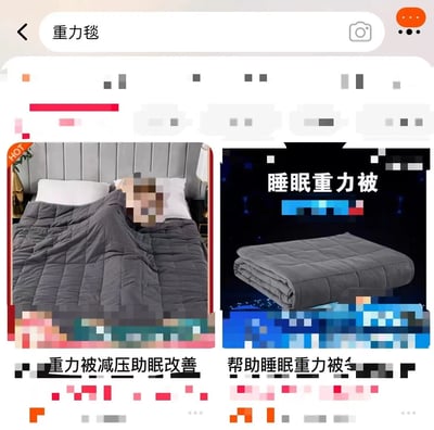 该图片为手机电商平台搜索“重力毯”的结果截图，展示了两款重力毯商品。左侧图片中，一张床上铺着灰色重力毯，床上有人但面部被像素化处理；右侧图片展示了折叠状态的灰色重力毯，上方有文字“睡眠重力被”。图片下方分别有商品描述文字“重力被减压助眠改善”和“帮助睡眠重力被”。界面顶部有搜索栏，显示搜索关键词“重力毯”。