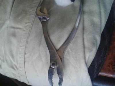 这是一张原始拍摄的静态单图，画面主体是一把金属材质的水泵钳（也叫鲤鱼钳），钳子的一端是可调节开口的钳头，另一端是带有齿纹的夹持端，整体呈现出使用过的金属质感，被放置在一块浅卡其色的布料表面，布料带有自然的褶皱，画面上方还有一小团类似棉花的白色物体。水泵钳是常见的手动五金工具，常用于夹持、拧动不规则或尺寸较大的零件，也可剪切较细的金属丝。
