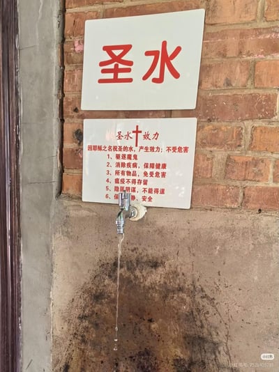 砖墙背景上安装着两块白色标牌，上方标牌用红色大字写着'圣水'，下方标牌详细列出'圣水效力'的六项功能：驱除恶鬼、消除疾病、保护物品、驱逐瘟疫、破除阴谋、保障安全。标牌下方有一个正在滴水的水龙头，水龙头下方的墙面因长期滴水已出现深色水渍。