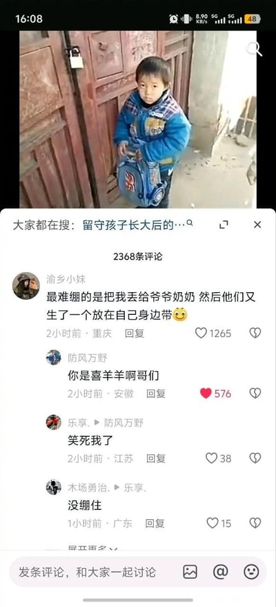 这张图是社交媒体内容截图，上方是实拍画面：一名穿着蓝色厚棉衣的小男孩背着蓝色书包，站在挂着锁的老旧红色木门旁，神情低落茫然，看起来是放学回家后发现家中无人被锁在门外。画面下方显示该内容关联的搜索提示为“大家都在搜：留守儿童长大后的…”，再下方是该内容的评论区：第一条热评来自用户“渝乡小妹”，内容为“最难绷的是把我丢给爷爷奶奶 然后他们又生了一个放在自己身边带”，搭配微笑表情；第二条评论来自用户“防风万野”，玩梗回复“你是喜羊羊啊哥们”，后续还有其他用户留言表示“笑死我了”“没绷住”。此处的梗源于动画《喜羊羊与灰太狼》的设定：喜羊羊的父母在外工作，将喜羊羊留在羊村交由长辈照顾，还生育了妹妹冰冰羊带在自己身边，刚好和热评描述的情况完全对应，形成了意料之外的搞笑效果。