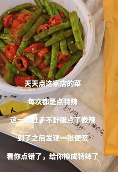 这是一张带有文字标注的实拍外卖图，画面主体是一份装在白色餐盒内的炒四季豆，菜品中混有大量红色辣椒段，看起来辣味十足。餐盒旁的塑料餐盒盖上有商家手写的便签。图上配文讲述了整件事的来龙去脉：发布者经常点这家店的特辣菜品，本次因为肚子不舒服特意点了微辣，结果收到餐时看到商家的便签，商家误以为发布者点微辣是操作失误，特意把餐品换成了特辣，整件事充满了哭笑不得的反差感。