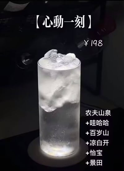 图片展示了一杯装在高脚杯中的饮品，杯中装有冰块和呈现云雾状的液体（疑似冰水混合物）。杯身上方有醒目标题【心動一刻】，右侧标注价格¥198，下方则列出原料：农夫山泉+哇哈哈+百岁山+凉白开+怡宝——均为市面上常见的平价饮用水品牌。

图片通过将普通饮用水混合后冠以“心动一刻”之名并标价198元，形成强烈反差，以此讽刺部分商家将简单商品包装成高价“网红产品”的营销现象，带有明显的幽默调侃意味。